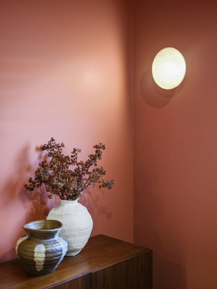 Terracotta painted wall with a globe sconce, ceramic vases and dried flowers on a timber sideboard