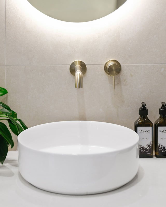 Brushed brass wall tapware above a round vessel basin