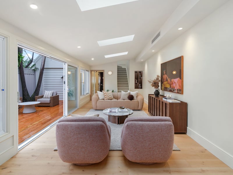 Living room with two curved pink armchairs under skylights, stacker doors open to a timber deck